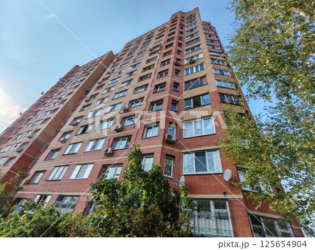 A modern apartment building with a red and beige brick facade, multiple windows, and balconies. This urban structure highlights the straightforward design and functionality of residential housing in 125654904