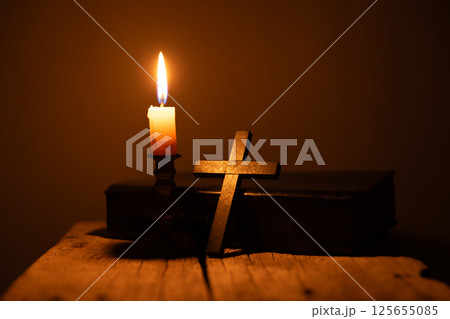 Light candle with holy bible and cross or crucifix on old wooden background in church.Candlelight and open book on vintage wood table christianity study and reading in home.Concept of christ religion 125655085