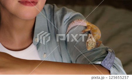 A gecko perched on a woman s shoulder looks outward, embodying curiosity and calm. The image connects with themes of exotic wildlife and respectful handling of unique creatures. A gecko perched on a woman s shoulder looks outward, embodying curiosity and calm. The image connects with themes of exotic wildlife and respectful handling of unique creatures. 125655257