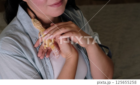 A leopard gecko rests securely in a woman s hands as she cradles it near her chest. This scene reflects the growing appreciation for reptiles as calming and unique companions. 125655258