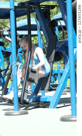 A woman in a blue sports outfit is engaged in a leg press workout at an outdoor gym, demonstrating focus and effort. This image emphasizes the significance of consistency in fitness and the pursuit of A woman in a blue sports outfit is engaged in a leg press workout at an outdoor gym, demonstrating focus and effort. This image emphasizes the significance of consistency in fitness and the pursuit of 125655266
