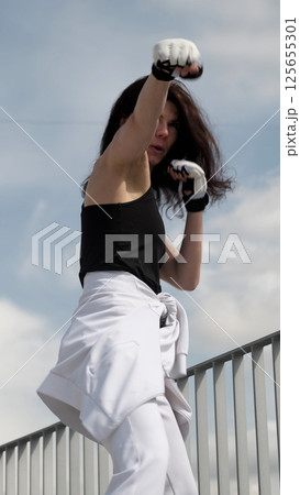 A determined woman in sports gloves throws a powerful punch, showcasing strength and focus. This image represents self-defense, fitness training, and empowerment. A determined woman in sports gloves throws a powerful punch, showcasing strength and focus. This image represents self-defense, fitness training, and empowerment. 125655301
