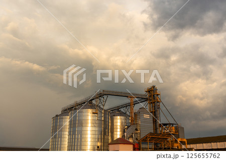 Group of grain dryers complex on dramatic cloudy sunset sky. 125655762