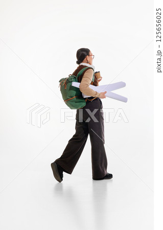 Back view of pensioner, elderly woman with green backpack and coffee cup walking against white background. Architecture student. 125656025