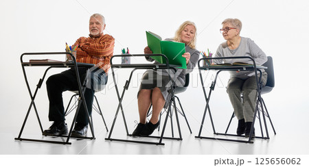 Elderly classmates sitting together sharing reading materials, exchanging ideas with curiosity and support against white background. Elderly classmates sitting together sharing reading materials, exchanging ideas with curiosity and support against white background. 125656062