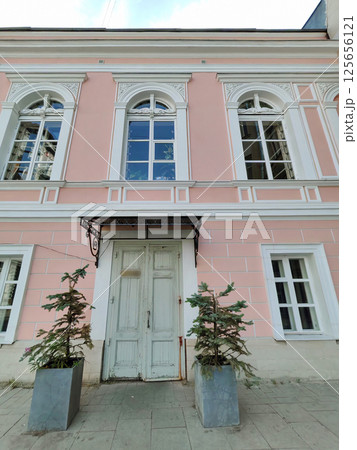 An old pink building facade with two small trees in pots by a weathered door. The faded charm reflects urban nostalgia and the slow decay of historic architecture. An old pink building facade with two small trees in pots by a weathered door. The faded charm reflects urban nostalgia and the slow decay of historic architecture. 125656121