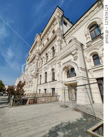 A white historic structure with decorative moldings, symmetrical arches, and modern barriers. This photo reflects the balance between cultural preservation and urban development. 125656124