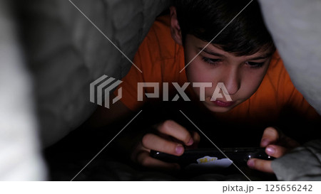 child is engrossed in his smartphone while tucked under a blanket, emphasizing the intimate and captivating moments of screen time in today s digital age. 125656242
