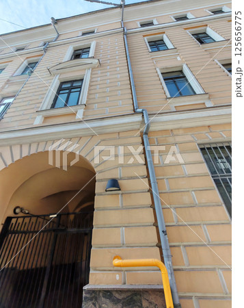 A textured facade of a beige building with symmetrical windows and a tall arched entry. The visible pipes and fixtures symbolize the coexistence of traditional style and modern utility. 125656775