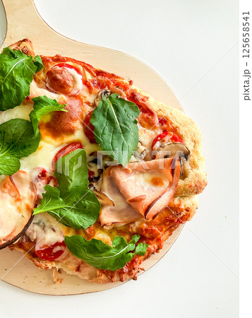 Fresh homemade pizza with basil, tomatoes, and ham toppings on wooden board 125658541
