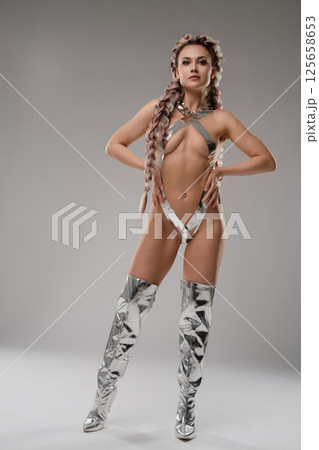 Woman in silver bodyart poses confidently in unique lingerie at a studio 125658653