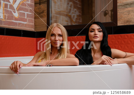Two women in lingerie posing elegantly beside a luxurious bathtub Two women in lingerie posing elegantly beside a luxurious bathtub 125658689