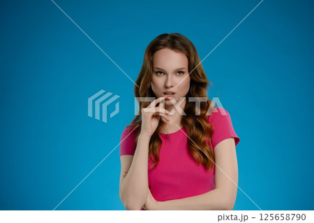 Woman with long hair expressing emotion while posing in a studio setting with a bright blue background Woman with long hair expressing emotion while posing in a studio setting with a bright blue background 125658790