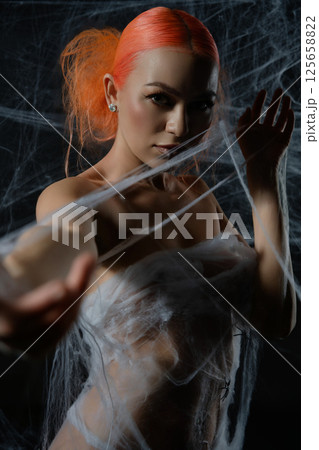 Red-haired woman ensnared in a delicate net trap amidst a dark background Red-haired woman ensnared in a delicate net trap amidst a dark background 125658822
