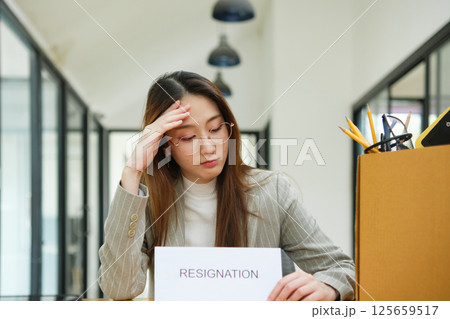Unemployed woman with resignation letter and office box showing stress after layoff 125659517