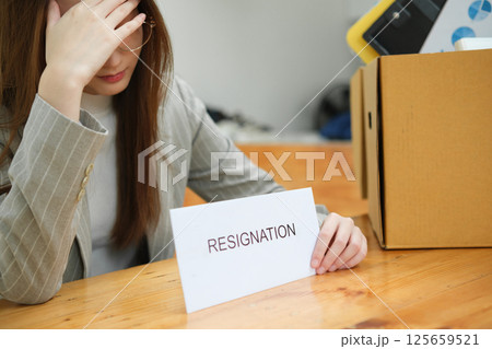 Unemployed woman with resignation letter and office box showing stress after layoff 125659521