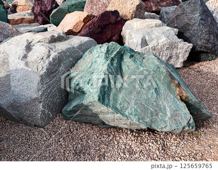 Stones of various colors and textures form a natural landscape. The image showcases a collection of diverse boulders, including green and gray stones, on a bed of gravel Stones of various colors and textures form a natural landscape. The image showcases a collection of diverse boulders, including green and gray stones, on a bed of gravel 125659765