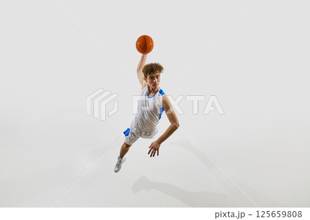 Aerial view photo of young male basketball athlete flying through air, arm raised to score final goal against white studio background. 125659808