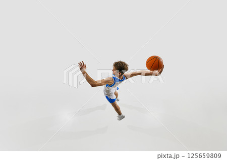 Basketball player jumping forward with explosive energy, one hand reaching back with ball, in motion, ready for final slam dunk. 125659809