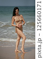 Happy cheerful 51 year old middle aged smiling woman in beige-gold swimsuit bikini standing on the beach near the sea and looking at camera 125660171