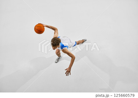 High angle basketball photo of young athlete in motion preparing scoring goal, running and leaping against white studio background. High angle basketball photo of young athlete in motion preparing scoring goal, running and leaping against white studio background. 125660579