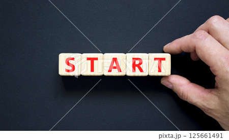 Start symbol. Concept word Start on beautiful wooden blocks. Beautiful black table black background. Businessman hand. Business lifestyle start concept. Copy space. Start symbol. Concept word Start on beautiful wooden blocks. Beautiful black table black background. Businessman hand. Business lifestyle start concept. Copy space. 125661491