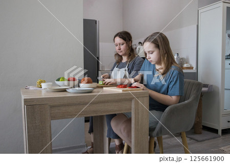 Attractive daughter and her mother cooking in domestic kitchen together, family lifestyle portrait 125661900