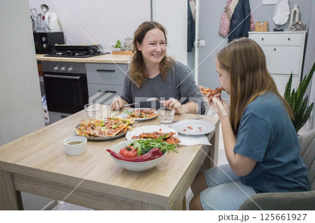 Mother and her daughter eating homemade pizza. Pretty mother and lovely girl having fun indoor Mother and her daughter eating homemade pizza. Pretty mother and lovely girl having fun indoor 125661927