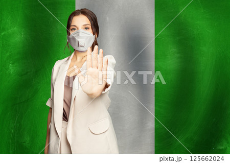 Confident woman in medical mask showing stop gesture open palm hand against flag Confident woman in medical mask showing stop gesture open palm hand against flag 125662024