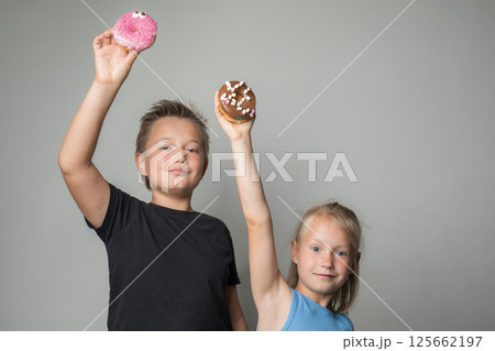 Smiling children holding chocolate glazed donut indoor. Happy kids with sweet food portrait 125662197