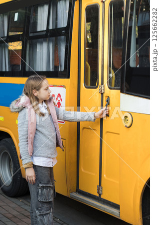 Pretty girl child school student opens the door of a school bus Pretty girl child school student opens the door of a school bus 125662282