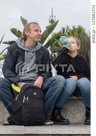 Smiling father and daughter child girl drinking water while sitting outdoors. Happy family Smiling father and daughter child girl drinking water while sitting outdoors. Happy family 125662551