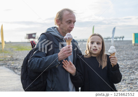 Laughing child daughter and her father walking and eating ice cream outdoors. Happy family Laughing child daughter and her father walking and eating ice cream outdoors. Happy family 125662552
