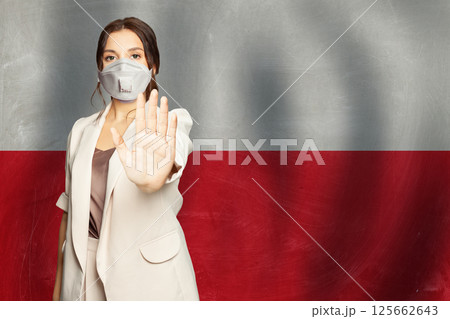 Confident woman in medical mask showing stop gesture open palm hand against flag of Poland  125662643