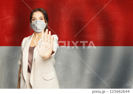 Serious woman in protective mask against Monaco flag banner background Serious woman in protective mask against Monaco flag banner background 125662644