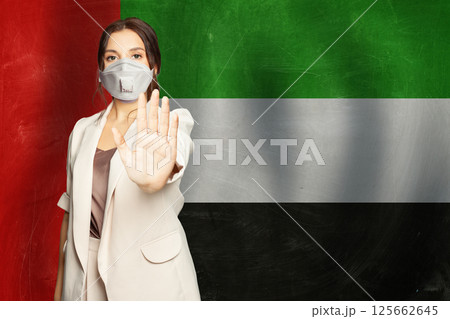 Confident woman in medical mask showing stop gesture open palm hand against flag  125662645