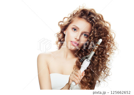 Isolated young model woman with long curly wavy hairstyle showing hot curling tongs iron 125662652