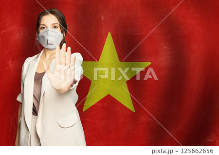 Confident woman in medical mask showing stop gesture open palm hand against flag of Vietnam Confident woman in medical mask showing stop gesture open palm hand against flag of Vietnam 125662656