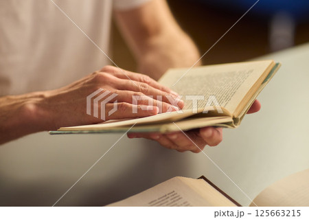 Hands purposefully engaged with an engrossing book carefully placed on a table surface 125663215