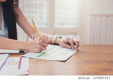 Close up of asian woman hand holding pencil analysis the graph at the home office for setting challenging business goals And planning to achieve the new target. Close up of asian woman hand holding pencil analysis the graph at the home office for setting challenging business goals And planning to achieve the new target. 125663351