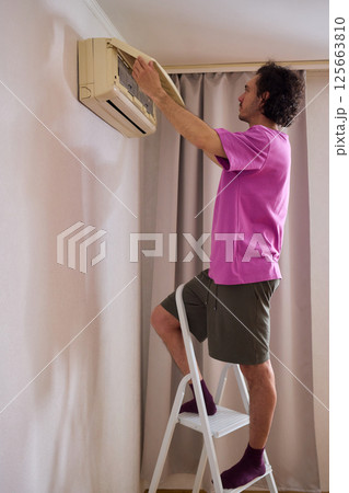 A person is diligently inspecting the filter of an air conditioning unit for optimal performance 125663810