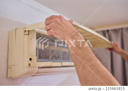 A person is diligently inspecting the filter of an air conditioning unit for optimal performance 125663815