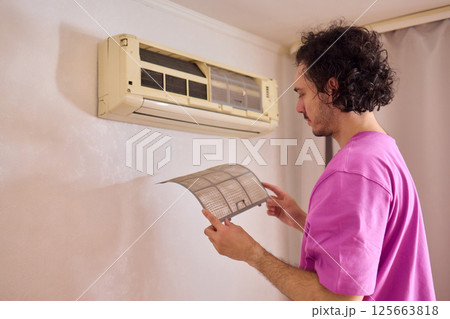 A person is diligently inspecting the filter of an air conditioning unit for optimal performance 125663818