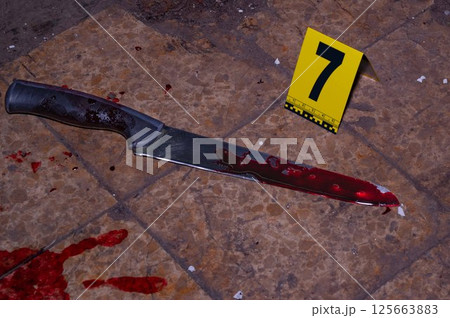 Bloody handprint and bloody knife at crime scene with yellow evidence marker 125663883