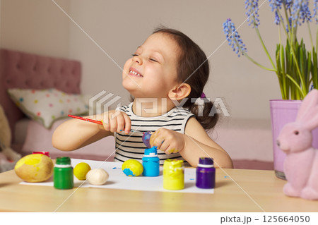 Little child girl paint Easter eggs at home. kid is preparing for Easter. 125664050