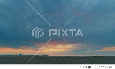 A Stunning Sunrise Displaying Vibrant Colors Over a Field Beneath a Dramatic Cloudy Sky 125664958