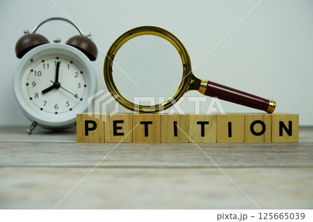 Magnifying glass and alarm clock with wooden blocks alphabet letters PETITION text message on wooden background Magnifying glass and alarm clock with wooden blocks alphabet letters PETITION text message on wooden background 125665039
