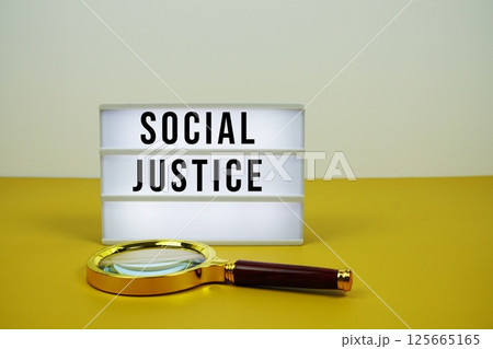 Social Justice text on LED lightbox with magnifying glass on yellow background 125665165
