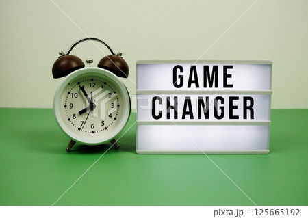 Game Changer text on LED lightbox with alarm clock on green background Game Changer text on LED lightbox with alarm clock on green background 125665192