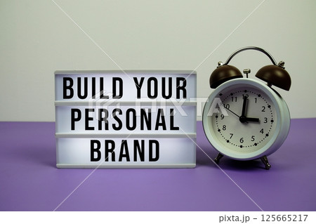 Build Your Personal Brand text on light box with alarm clock on purple background Build Your Personal Brand text on light box with alarm clock on purple background 125665217